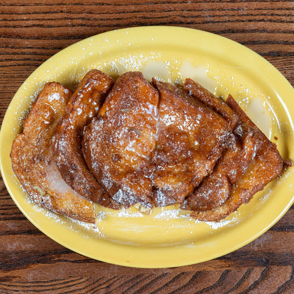 Golden brown French toast drizzled with glaze and powdered sugar on a yellow plate.