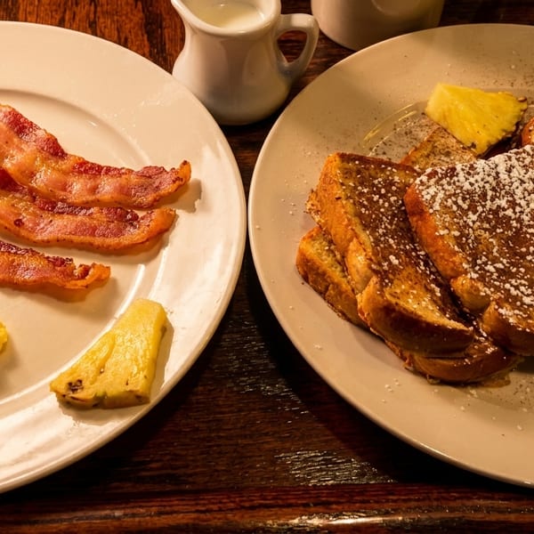 Hearty breakfast plates with scrambled eggs, crispy bacon, powdered French toast, and pineapple slices.