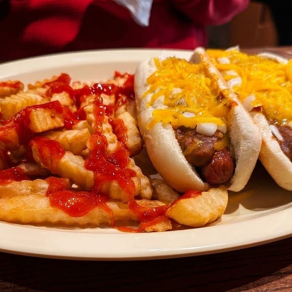 Two chili cheese hot dogs with diced onions and crinkle-cut fries with ketchup on a white plate.