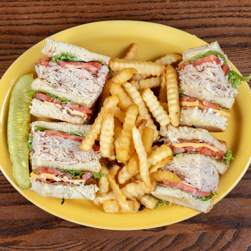 Classic club sandwich with crinkle-cut fries and a pickle spear on a yellow plate.