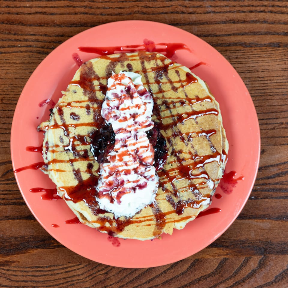 Waffle on a coral plate, topped with whipped cream, berry compote, and strawberry drizzle.