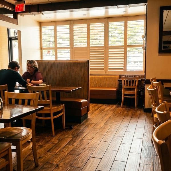 Cozy restaurant interior with two people at a booth and empty wooden tables.
